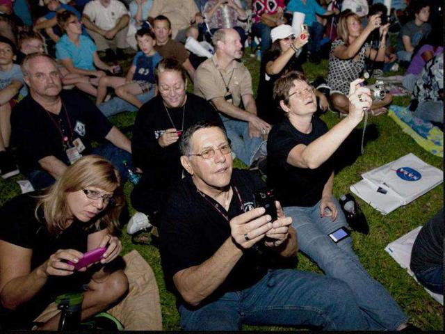 Nasa employee Jerry Davison, center, and his wife, Maureen, right, take photos as they watch at Johnson Space Center in Houston as space shuttle Atlantis approaches for landing at Kennedy Space Center.