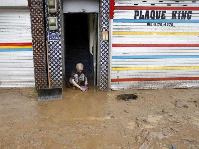 A man scrapes mud off the entrance of his residence in a street covered by mud after heavy rains near the US military base, Camp Casey in Dongducheon, north of Seoul, South Korea.