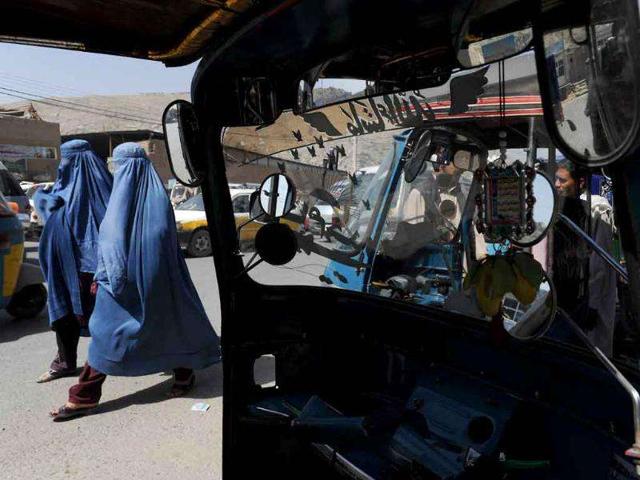 Two burqa-clad Afghan women walk past an auto-rickshaw in Kabul.
