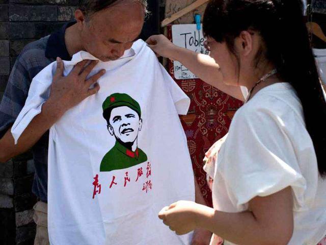 A Chinese woman helps a man as he holds a T-shirts with an image of US President Barack Obama dressed in a Cultural Revolution-era military uniform at a shop in Beijing.
