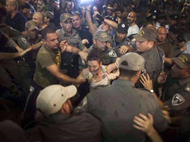 Israeli policemen try to arrest a young woman after protestors blocked a main junction following a protest march against rising housing prices and social inequalities in Tel Aviv.