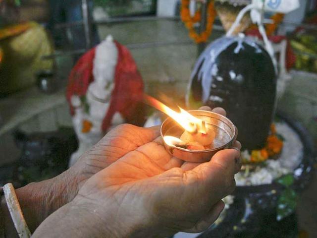A devotee holds an oil lamp next to a Shivling (a symbol of Lord Shiva) as she worships during the Naag Panchami festival at a temple in Chandigarh.