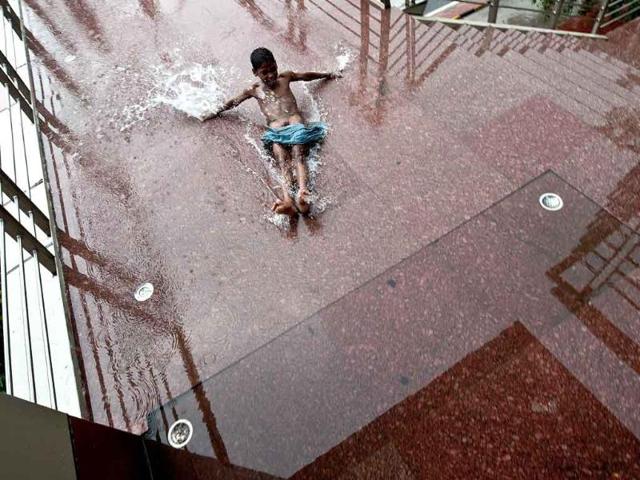 A homeless child slides in a puddle on a foot-over bridge during heavy rainfall in New Delhi.