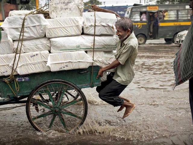 A man tries to keep his feet above the water as he clings on the back of a bicycle cart at a water-logged intersection during monsoon rain in New Delhi.