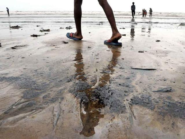Beachgoers walk on the oil covered shores of Juhu Chowpatty beach in Mumbai. Authorities worked to clean up an oil spill from a cargo ship that sank off Mumbai last week, with oil found on beaches and in water near the city's shoreline.