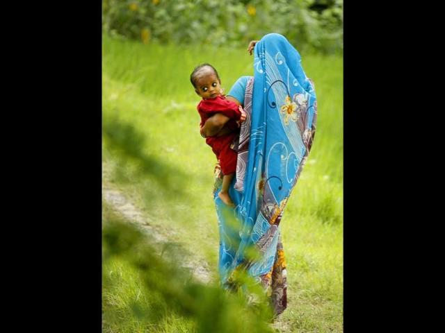 Woman holds a child and walks through a paddy field in Pawara village, Allahabad. Woman holds a child and walks through a paddy field in Pawara village, Allahabad.