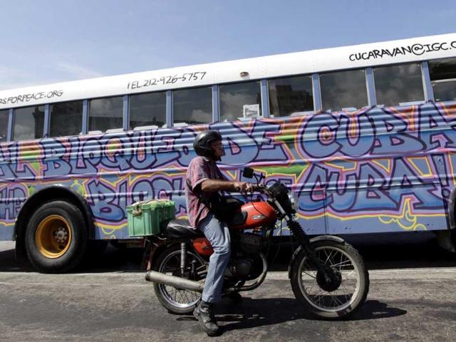 A man on a motorcycle waits at traffic lights beside a bus donated by the Pastors of Peace adorned with graffiti demanding an end to the US trade embargo on Cuba in Havana.