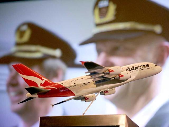 A model Qantas aeroplane sits on the stage as a photo of a Qantas employee is projected onto a screen during the release of company full-year results in Sydney.