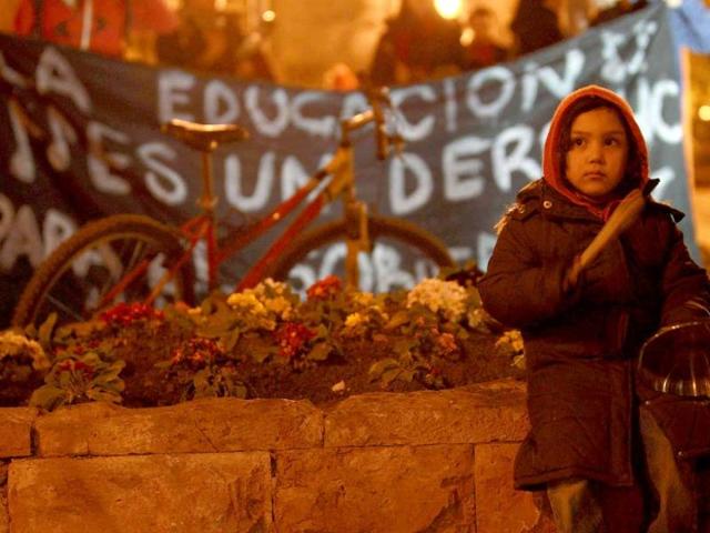 A child beats cooking utensils in front of a banner that reads The education is a right during a rally to demand changes in the public state education system, at Santiago.