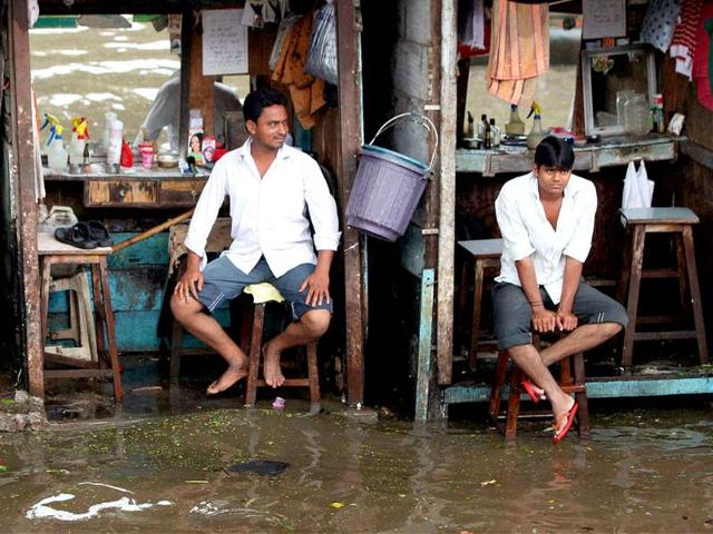 Barbers wait for coustomers at their shops along a flooded road after heavy downpour in Mumbai.