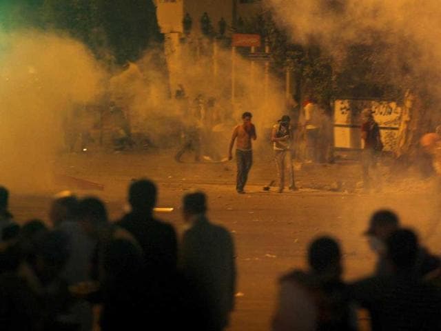 Protesters throw stones as tear gas is seen around them during clashes with Egyptian security forces next to a building housing the Israeli embassy in Cairo, Egypt.