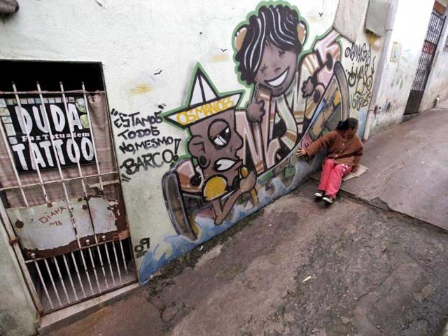A woman sits next to graffiti painted by artists working with OPNI, an organization that uses graffiti to improve life in the slums, in the Vila Flavia favela of Sao Paulo.