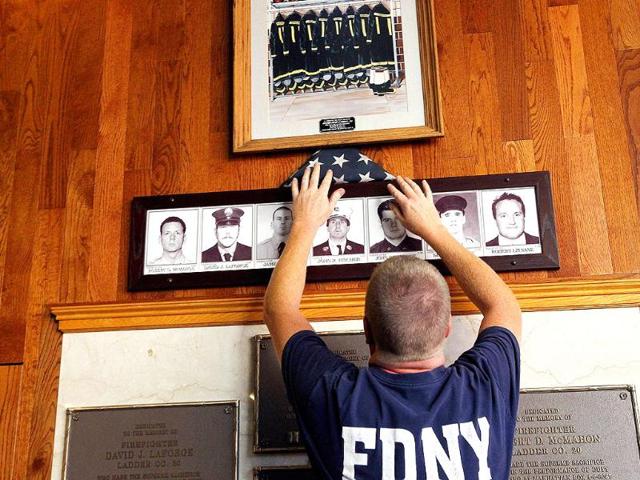 A firefighter places an American flag on a memorial display while preparing for 9/11 ceremonies at FDNY Ladder 20 Engine 13 on in New York City.