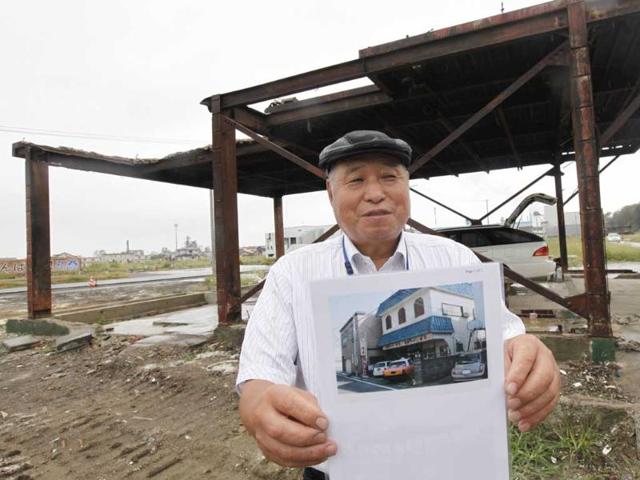 Katsuju Okata holds up a picture of his restaurant taken before it was destroyed by the March 11 earthquake and tsunami, as he stands in front of what remains of it in Ishinomaki, Miyagi Prefecture, six months after the disaster.