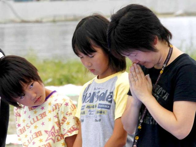 A girl looks at her mother who is observing a minute of silence for victims of the 9.0 magnitude earthquake and tsunami on March 11 in Ishinomaki, Miyagi Prefecture, six months after the area was devastated by the disaster.