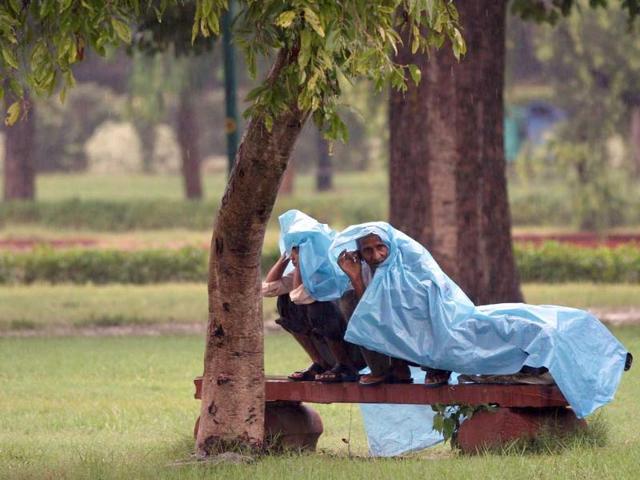 Men cover themselves with a plastic sheet to get protection from the rain at India Gate Lawns in New Delhi.