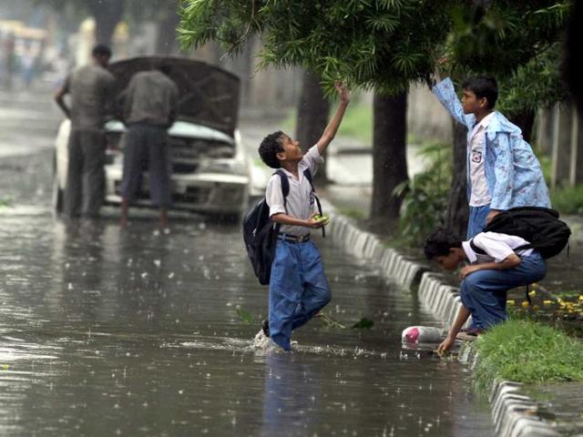 Students enjoy themselves on their way back from school through water logged streets at Inderpuri in west Delhi.