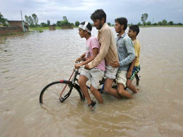 Men ride on a bicycle through a flooded road after a heavy downpour on the outskirts of Jammu.
