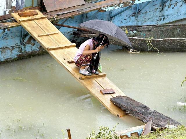 A Kashmiri girl carrying an umbrella crosses a pathway from her houseboat on Jehlum River to shore during rainfall in Srinagar.