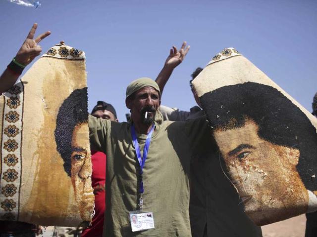 A former rebel fighter holds pieces of a carpet with the image of Muammar Gaddafi at a checkpoint in Wadi Dinar, Libya.