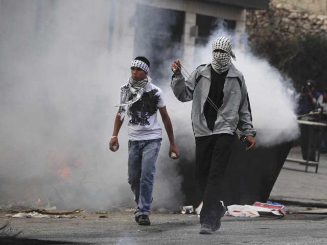 Palestinian demonstrators carry a slingshot and rocks past a burning trash bin during clashes with Israeli soldiers, during a protest at the Qalandia checkpoint between the West Bank city of Ramallah and Jerusalem.