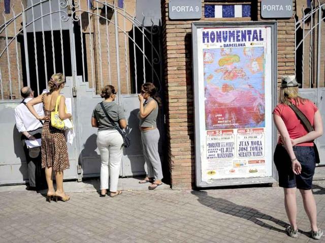 People wait at a main entrace next to a poster of Catalonia's final bullfight at the Plaza Monumental bullring in Barcelona.