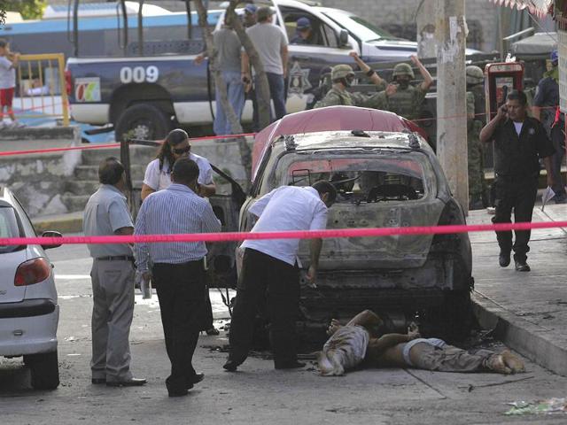 Police and forensic workers stand next to the dead bodies of two men at a crime scene in Acapulco.