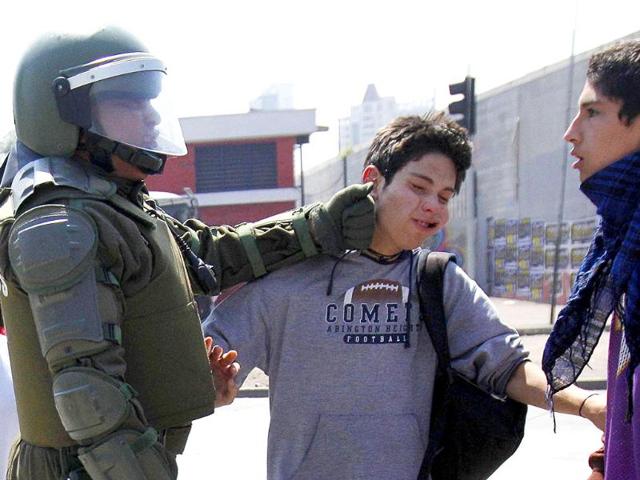 A riot police officer punches a student during a protest against the government and the public state education system at Santiago city.