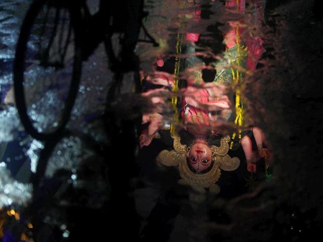 An idol of goddess Durga is reflected in a puddle created by rain water at a street during Durga Puja festival in Hyderabad.