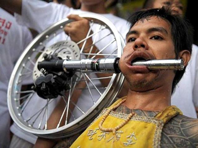 A devotee of the Chinese Bang Neow Shrine sits with a shock absorber piercing his cheek ahead of a street procession to mark the annual Vegetarian Festival in the southern Thai town of Phuket.