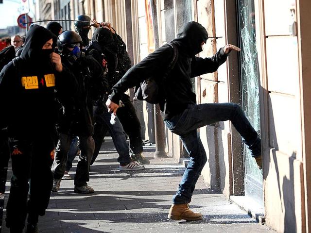 A protester breaks the window of a bank during a demonstration, in dowtown Rome.