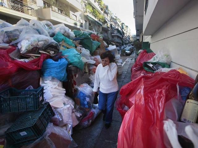 A woman covers her nose as she walks by a wall of pilling garbage during the second week of a strike by municipality workers and garbage collectors in Athens. Greek unions began a 48-hour general strike, the biggest protest in years.