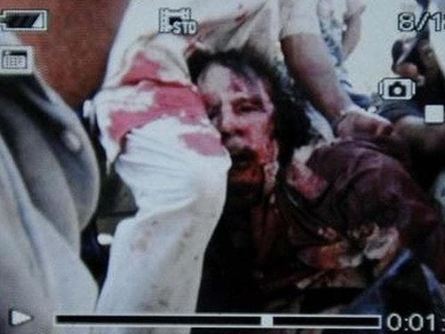 Former Libyan leader Muammar Gaddafi, covered in blood, is held on a truck by NTC fighters in Sirte in this still image taken from video footage.