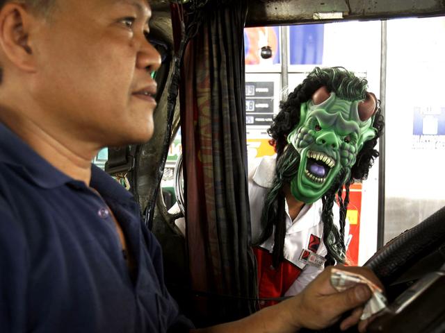 A gas station attendant wears a mask as part of their holiday treat as he talks to the driver of a commuter jeep Saturday, in suburban Mandaluyong City, east of Manila, Philippines. Attendants in the gas station wore masks to attract customers as Filipino Catholics prepare to observe All Saints' Day.