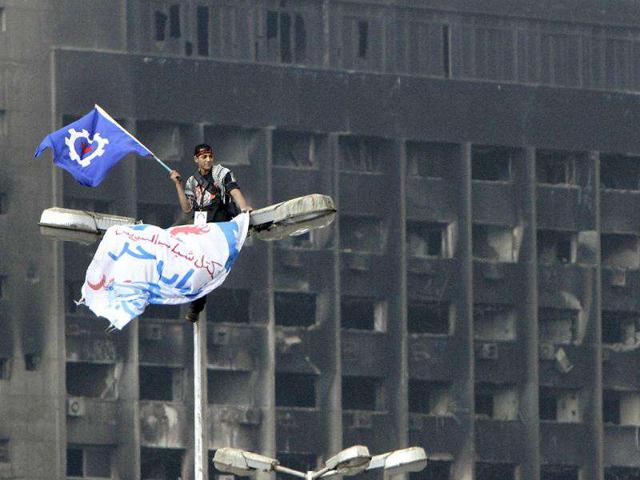An Egyptian protester waves banners as he climbs a lamp post in front of the former ruling National Democratic Party building which was damaged during a rally to protest against what they claim are attempts by the country's military rulers to reinforce their powers, Tahrir Square, Cairo, Egypt.