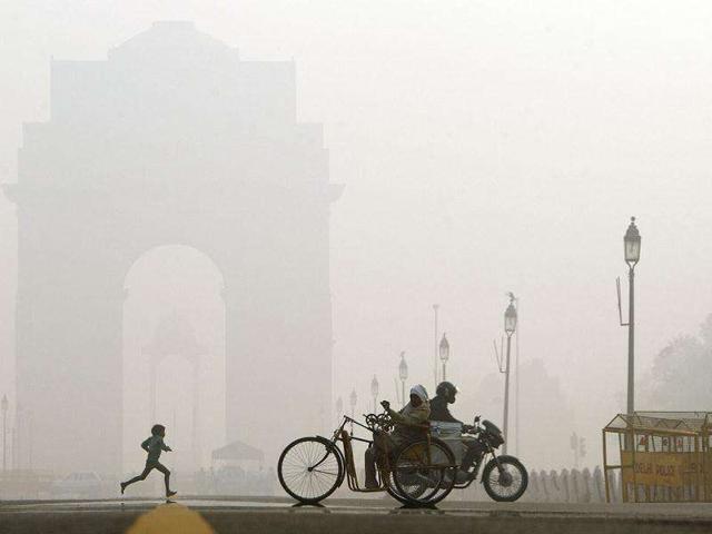 Commuters go past as a young child runs near India Gate, the war memorial in the morning fog, in New Delhi.