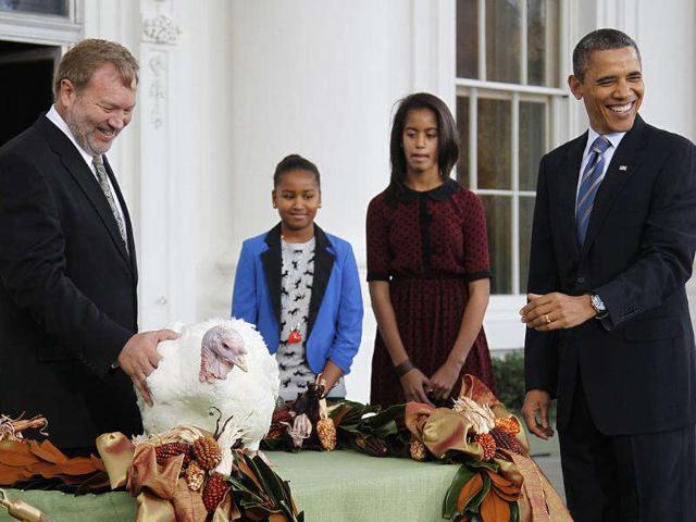 US President Barack Obama (R) reacts to the crowd as he pardons the 2011 Thanksgiving Turkey, Liberty, alongside his daughters Sasha (2nd L) and Malia, on the North Portico of the White House.