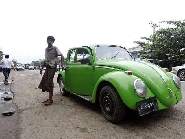 A man stands next to an old vehicle outside the vehicle license office as he waits to exchange it for a permit to import a newer car in Yangon.