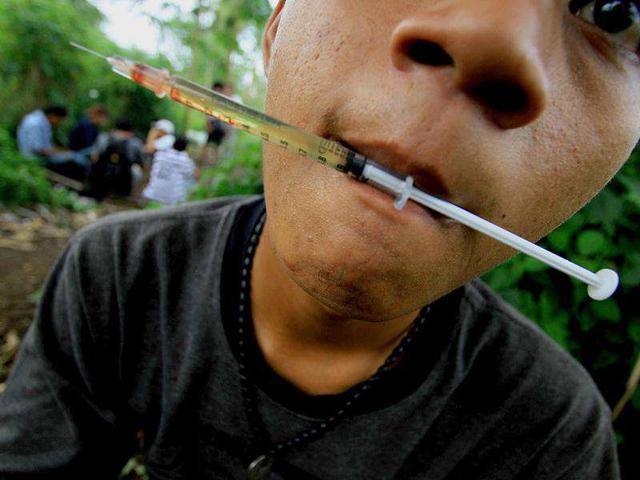 A heroin drug user holds a syringe in his mouth at a park in Medan city in Sumatra island. Cordia-Caritas Medan, an NGO, focuses on rehabilitation of heroin-users as part of its anti-HIV/AIDS campaign in Indonesia where the highest rate of HIV/AIDS infection comes from drug injection.
