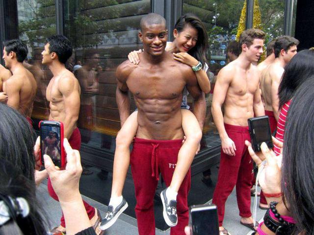 A woman poses with a shirtless model outside a department store in Singapore's Orchard Road shopping district. Shirtless men clad in red sweatpants have been lining up for days as part of an advertising gimmick revealing not just muscle but also a gradual unpeeling of the city state's puritanical ways. Reuters Photo