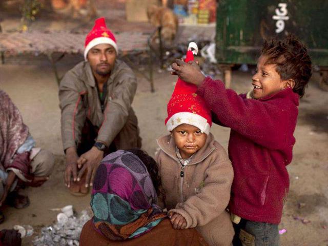 A boy adjusts a festive hat on another as they sit around a fire with their parents who are homeless street vendors at a Christmas market near the Sacred Heart's Cathedral in New Delhi. AP Photo/Kevin Frayer