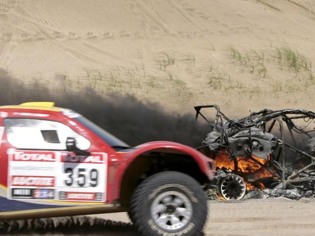 Driver Mark Corbett and co-driver Francois Jordaan, both from South Africa, race their Century Racing car past a burning Volvo car during the first stage of the 2012 Argentina-Chile-Peru Dakar Rally between Mar del Plata and Santa Rosa de la Pampa, Argentina.
