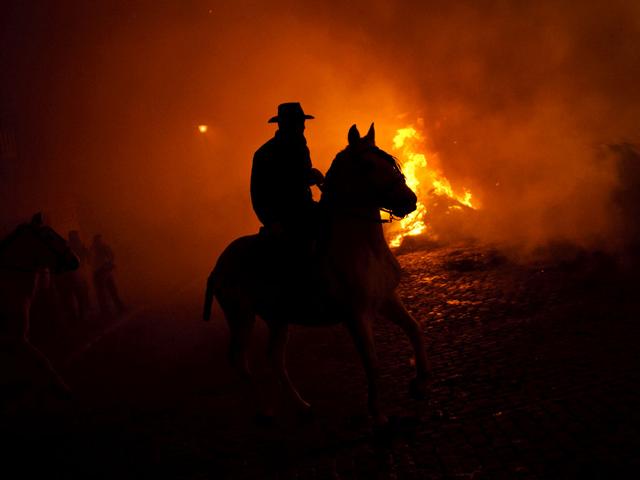 A man rides a horse near by a bonfire in San Bartolome de Pinares, Spain, in honor of Saint Anthony, the patron saint of animals. On the eve of Saint Anthony's Day, hundreds ride their horses trough the narrow cobblestone streets of the small village of San Bartolome during the 'Luminarias' a tradition that dates back 500 years and is meant to purify the animals with the smoke of the bonfires and protect them for the year to come. (AP Photo/Daniel Ochoa de Olza) A man rides a horse near by a bonfire in San Bartolome de Pinares, Spain, in honor of Saint Anthony, the patron saint of animals. On the eve of Saint Anthony's Day, hundreds ride their horses trough the narrow cobblestone streets of the small village of San Bartolome during the 'Luminarias' a tradition that dates back 500 years and is meant to purify the animals with the smoke of the bonfires and protect them for the year to come. (AP Photo/Daniel Ochoa de Olza)