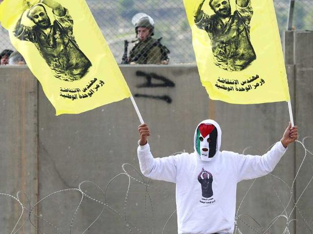 A masked Palestinian holds flags with the image of an imprisoned Palestinian leader Marwan Barghouti during a protest against Israel's separation barrier in the West Bank village of Bilin, near Ramallah. The poster reads: "The engineer of the Intifada, the symbol of unity". AP Photo/Nasser Shiyoukhi