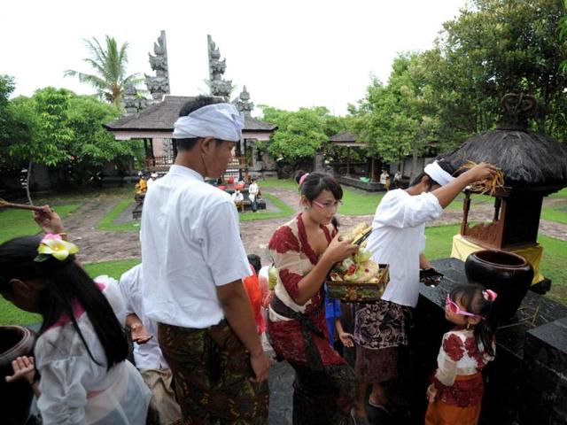 A Balinese Hindu devotee sprinkles holy water (R) as a woman (C) carries offerings during the celebration of the religious festival of Galungan at Jagatnatha temple in Singaraja, on the Hindu majority island of Bali. Galungan, based on the Hindu saka calendar, is the most important festival in Bali and symbolizes the victory of Virtue (Dharma) upon Evil (Adharma). AFP Photo /Sonny Tumbelaka