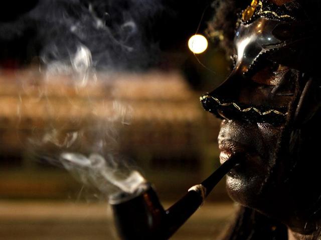 A man in a black Indian warrior costume smokes a pipe during a traditional mas competition in Victoria Square, Port of Spain. Reuters/Andrea De Silva