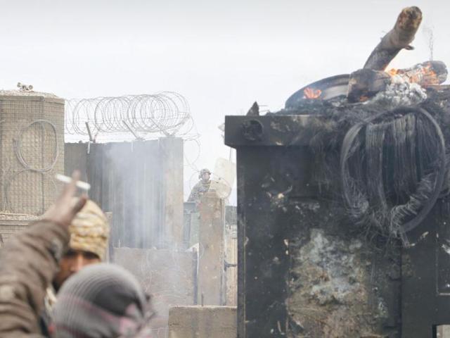 An Afghan protestor shouts slogans near burning security booth in front of the US base of Bagram during an anti US demonstration in Bagram north of Kabul