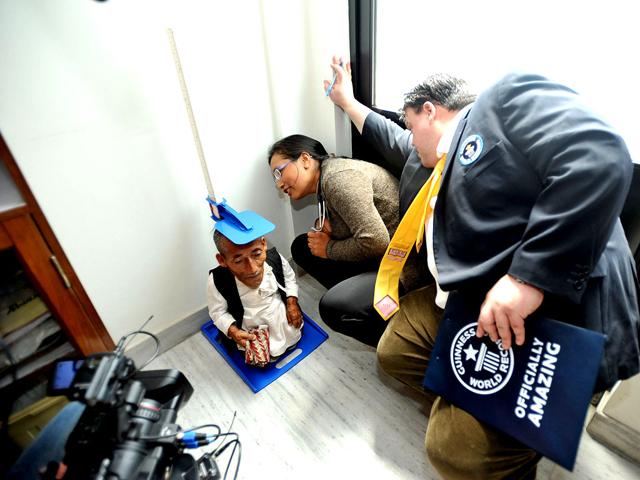 Chandra Bahadur Dangi, a 72-year-old Nepali only 21.5 inches (54.6 centimeters) tall, stands on a measuring device as medical doctor Rashila Pradhan (C) and Guinness World Records adjudicator Craig Glenday (R) look on at a hospital at Kathmandu. Dangi left his home in an isolated village in southwestern Nepal to fly to the capital, Kathmandu, to be measured by Guinness World Records officials. (AFP Photo/Prakash Mathema)