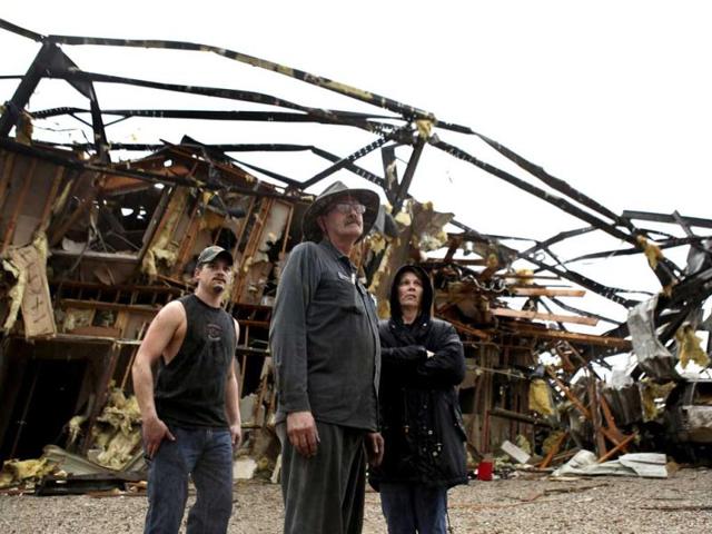 From left, Amos Calloway, Steve Burnett and his wife Rhonda Burnett look towards the hills after a tornado ripped through the Burnett's welding business outside of New Pekin, Indiana. Authorities in Indiana say at least ten people have been killed in violent storms that spawned tornadoes across a wide swath of southern Indiana. (AP Photo/The Courier-Journal, Matt Stone)
