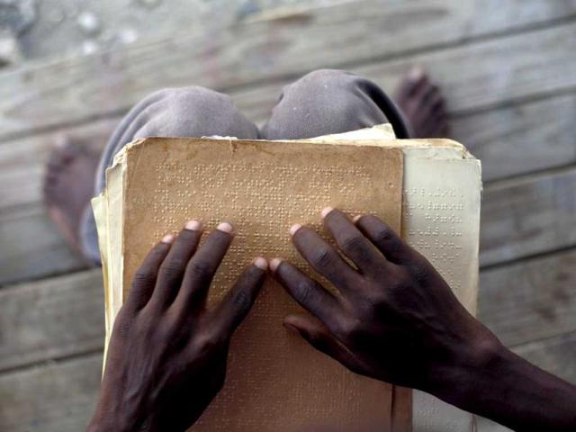 Joseph Clodise, 25, with visual disabilities reads in Braille at the entrance of his home at La Piste camp in Port-au-Prince, Haiti. AP Photo/Ramon Espinosa